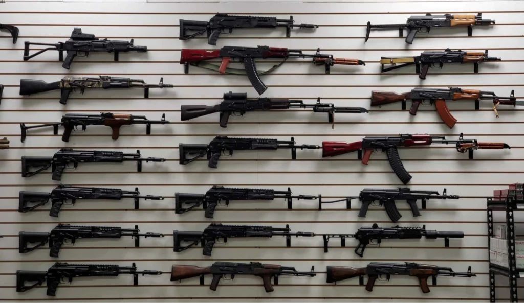 A wall display featuring multiple rifles with wooden and black finishes, arranged in rows on horizontal slats. The rifles vary slightly in size and style but share a similar design.