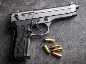 A semi-automatic handgun lies on a gray textured surface, with four bullets positioned nearby. The image is captured from an overhead perspective, highlighting the firearm's metallic details and grip design.