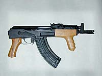 A compact assault rifle with a wooden foregrip and pistol grip, black metal body, and curved magazine, displayed against a plain light background.