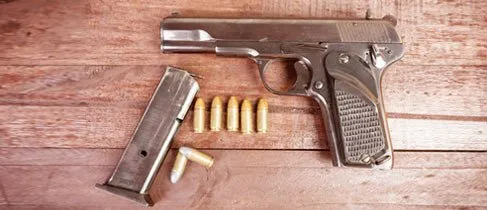 A silver handgun, a magazine, and seven bullets are displayed on a wooden surface.